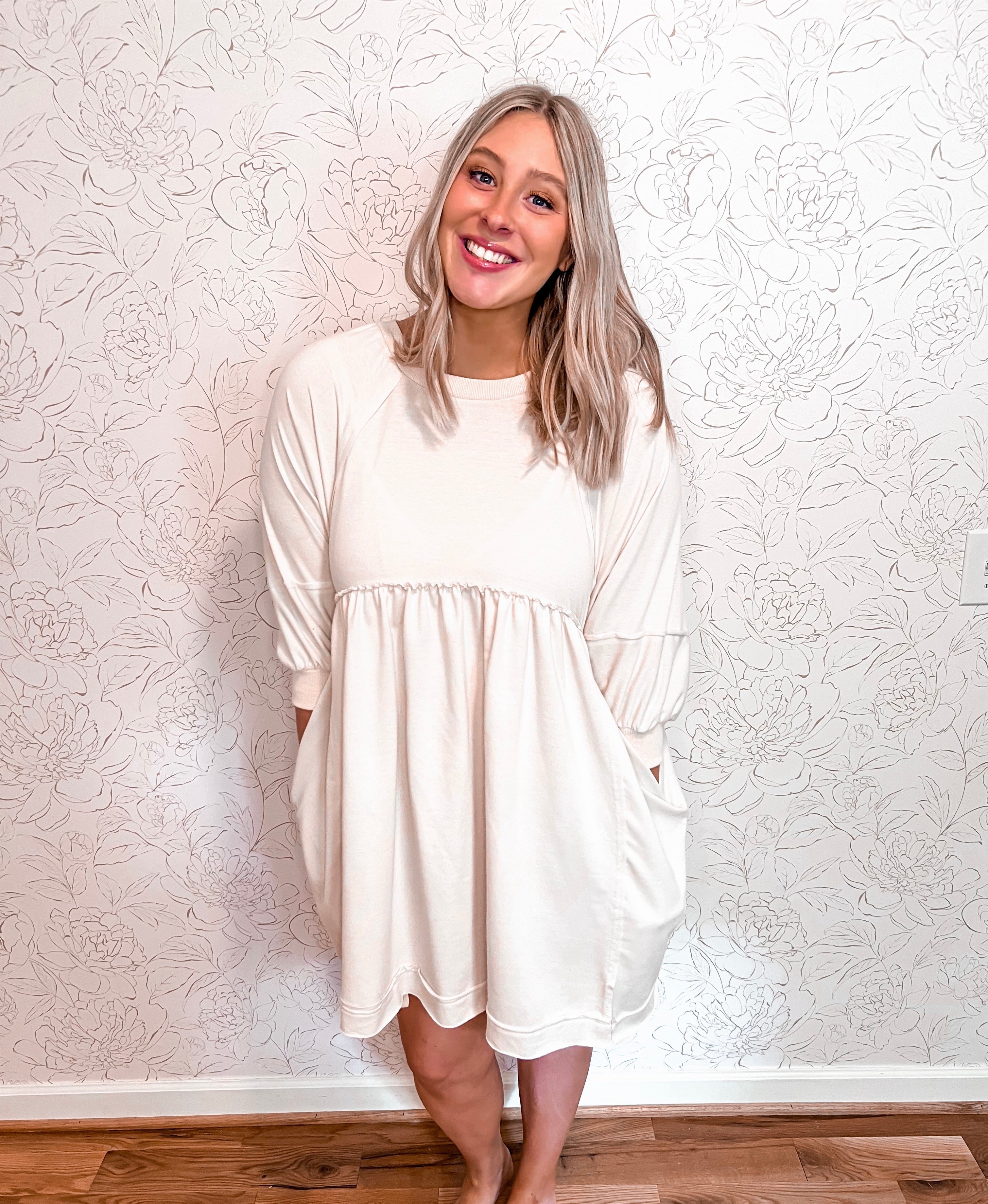 Oversized mini dress in a neutral oatmeal color, featuring quarter-length sleeves and deep pockets for functionality and style. The dress offers a roomy and comfortable fit, ideal for relaxed wear. Its minimalist design and soft hue make it versatile, easily styled for various occasions and suitable for all seasons