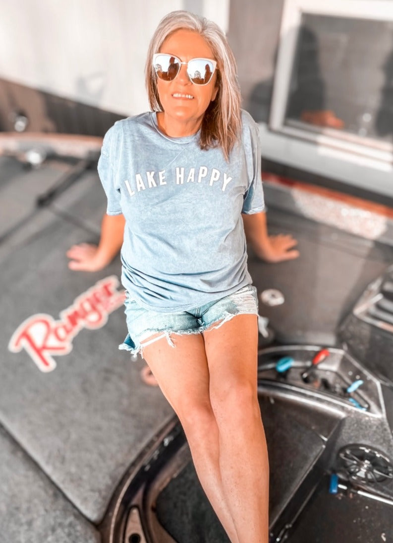 A mineral-washed blue graphic tee with the phrase 'Lake Happy' printed across the chest in white letters. The rich blue hue evokes the refreshing feel of summer by the water. The shirt's comfortable fit and inviting color make it an ideal choice for warm, laid-back days at the lake