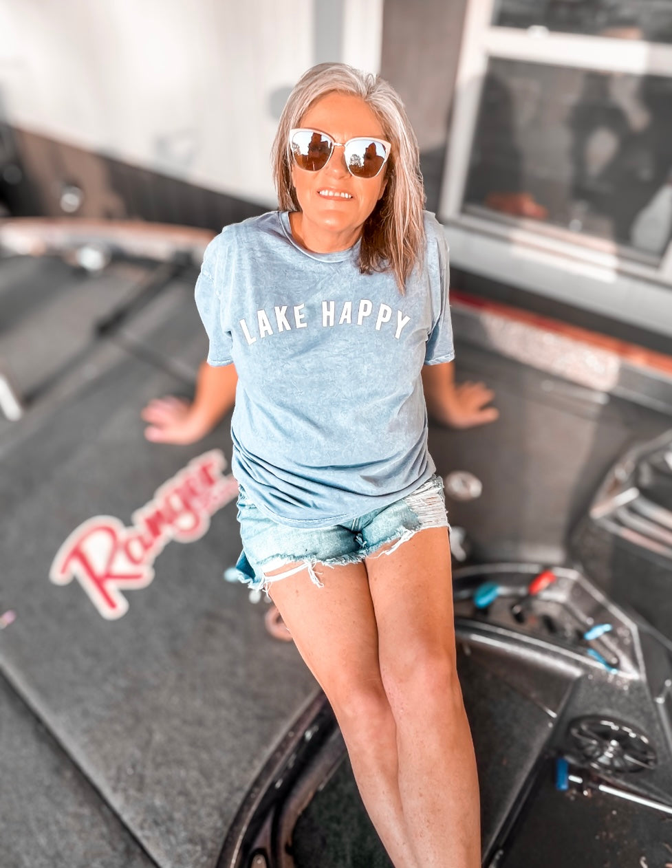 A mineral-washed blue graphic tee with the phrase 'Lake Happy' printed across the chest in white letters. The rich blue hue evokes the refreshing feel of summer by the water. The shirt's comfortable fit and inviting color make it an ideal choice for warm, laid-back days at the lake