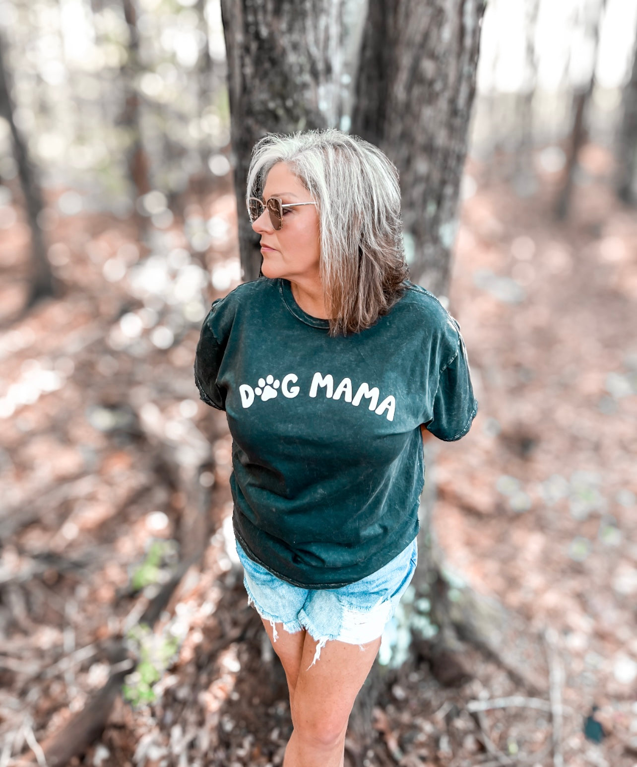 A black mineral-washed graphic tee with the phrase 'Dog Mama' prominently displayed in white puff print across the chest. The 'O' in 'Dog' is cleverly replaced with a white paw print, adding a playful touch to the design. The tee is crafted from a super soft and comfortable material, offering both style and comfort for dog lovers.