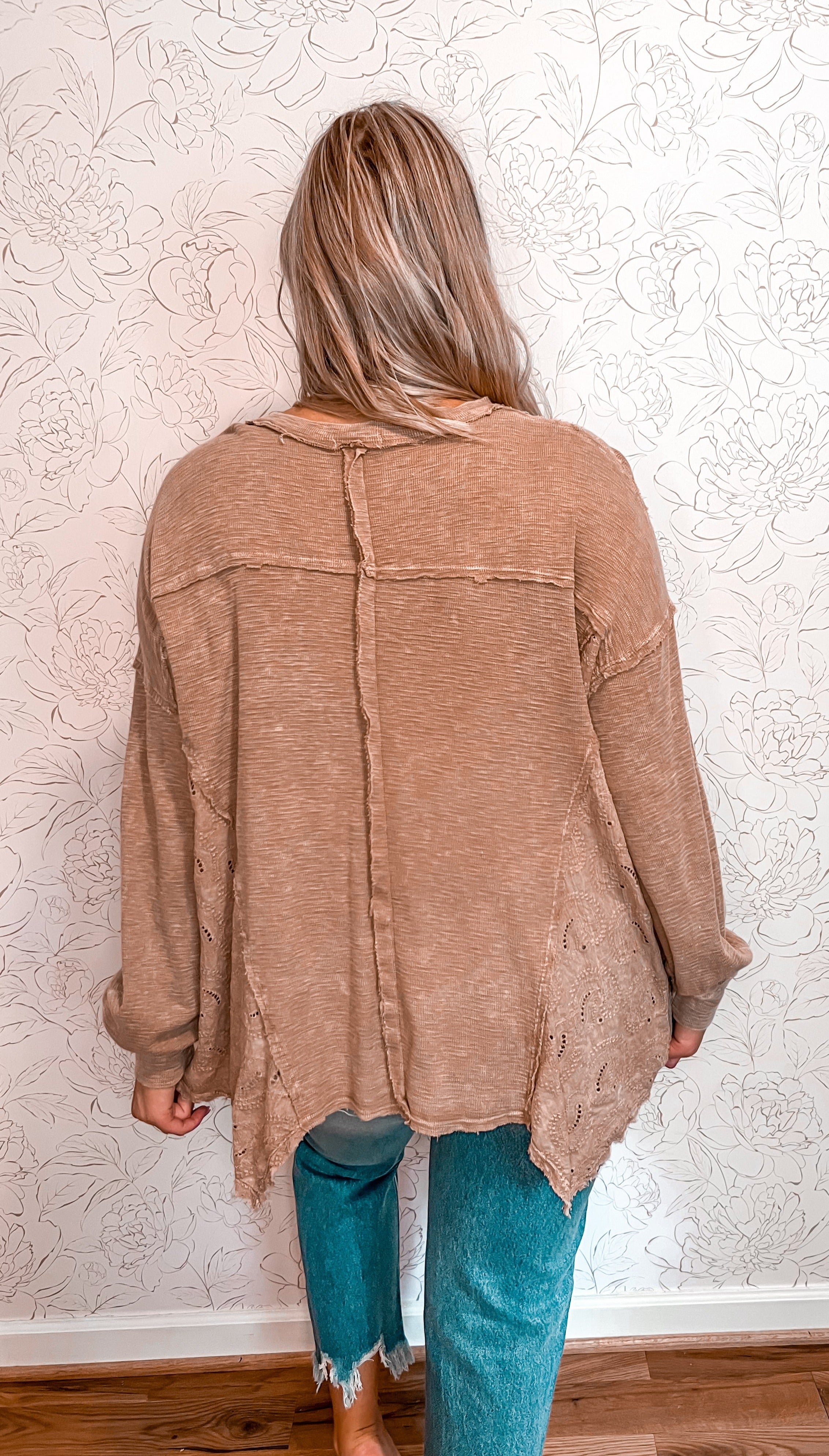 Long sleeve boho top featuring intricate paisley eyelet detailing along the sides, adding a decorative touch. The top has an uneven hem and slight distressing throughout, enhancing its rustic and free-spirited aesthetic. The design elements combine to offer a stylish, vintage-inspired look, perfect for those who appreciate unique and artistic clothing styles