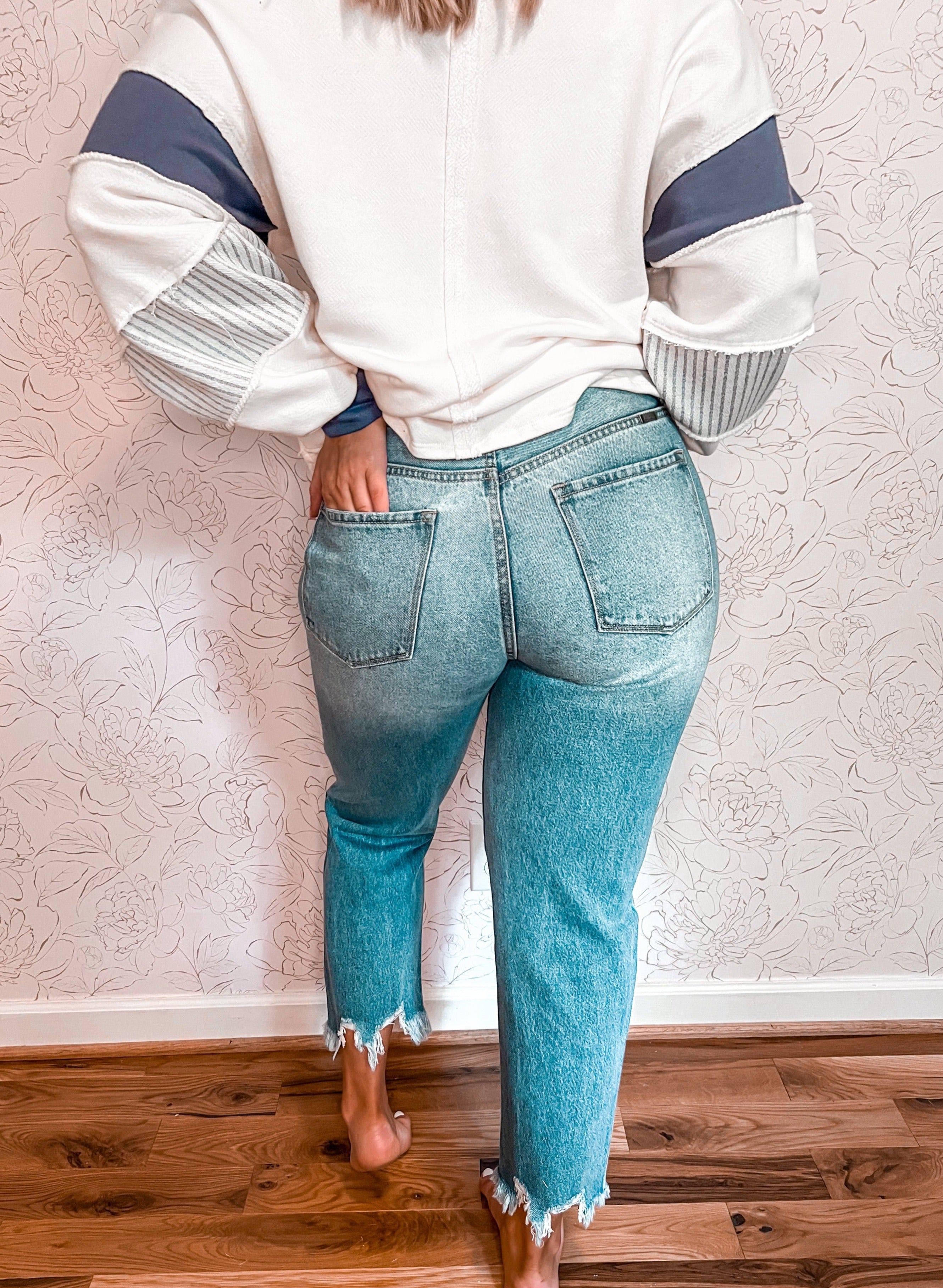 High-rise vintage mom jeans by KanCan, inspired by 90's fashion, featuring deliberate distressing for a lived-in look. These ankle-length jeans boast a classic, slightly tapered fit reminiscent of the era, with frayed edges around the pockets and hems for added character. The light to medium wash enhances their vintage appeal, making them a versatile piece for casual wear.